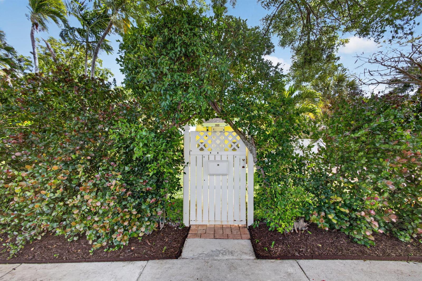 A white wooden gate with a mailbox is framed by lush green hedges and trees — 502 49th Street, West Palm Beach FL 33407, WEST PALM BEACH, FL