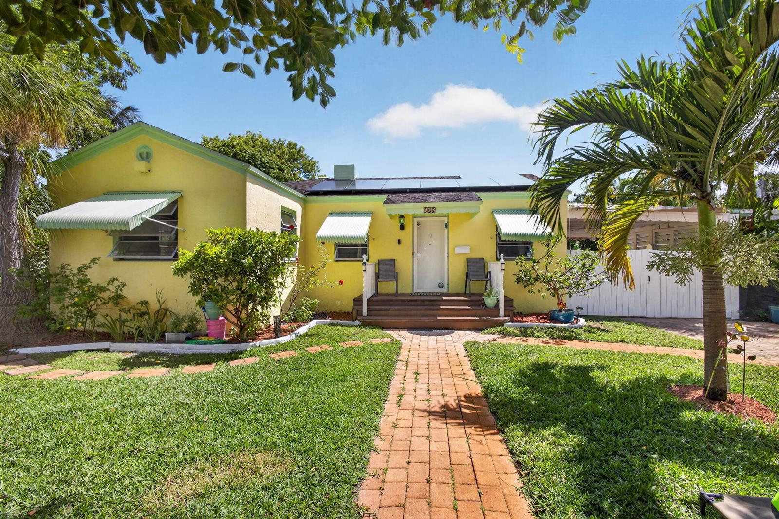 A yellow house with a brick walkway, green awnings, and solar panels on the roof — 502 49th Street, West Palm Beach FL 33407, WEST PALM BEACH, FL