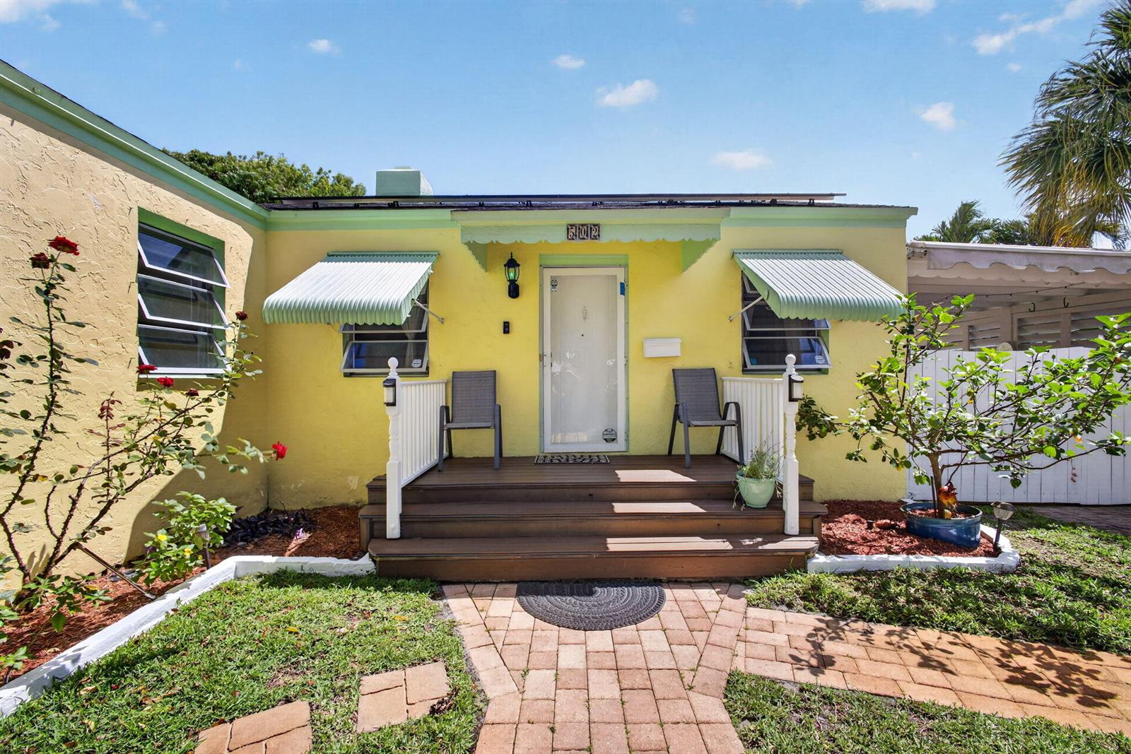 A yellow single-story house features a wooden front porch, green awnings, and a brick walkway — 502 49th Street, West Palm Beach FL 33407, WEST PALM BEACH, FL