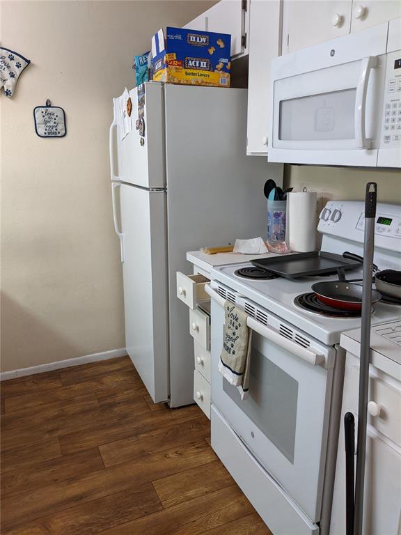 A kitchen features white appliances, wooden flooring, and a small set of drawers beside the stove — 4000 SW 23RD STREET UNIT 5-106, GAINESVILLE, FL