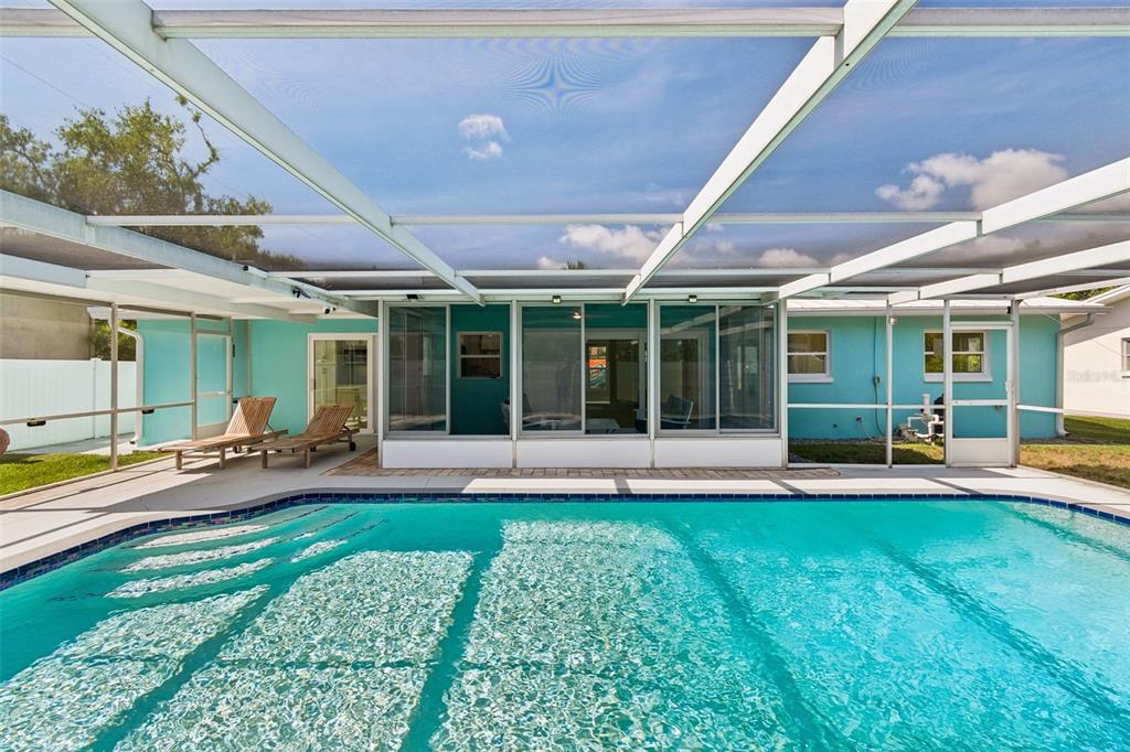 A swimming pool sits in front of a turquoise house with a screened-in patio area — 4388 50TH PLACE S, ST PETERSBURG, FL