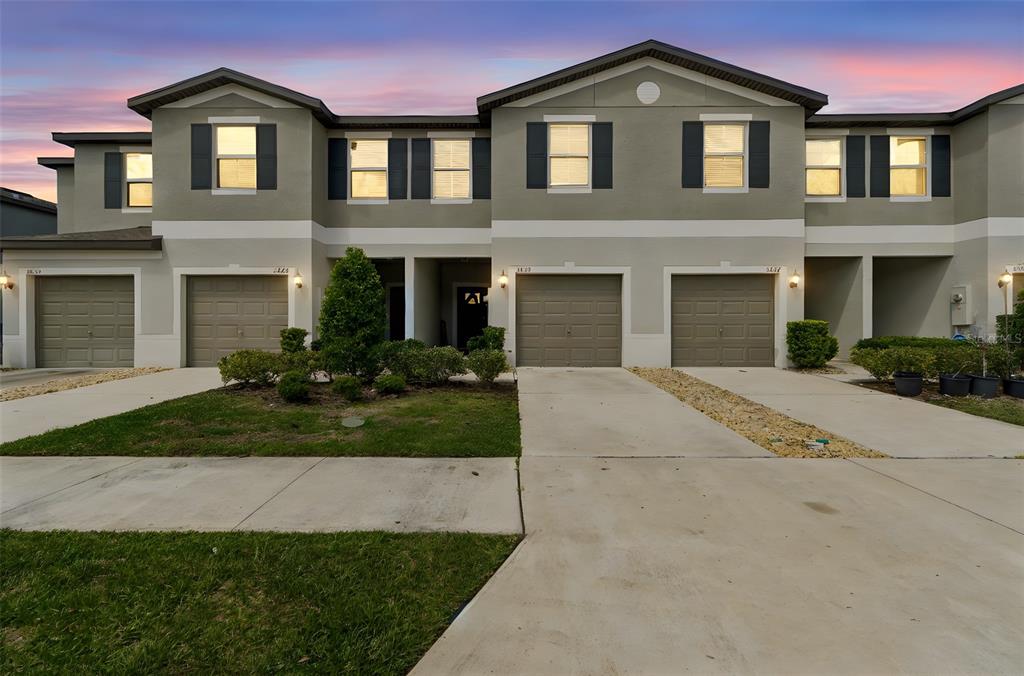 A row of multi-story townhouses with attached garages and concrete driveways under a sunset sky — 3633 BELLMEADE COURT, WESLEY CHAPEL, FL
