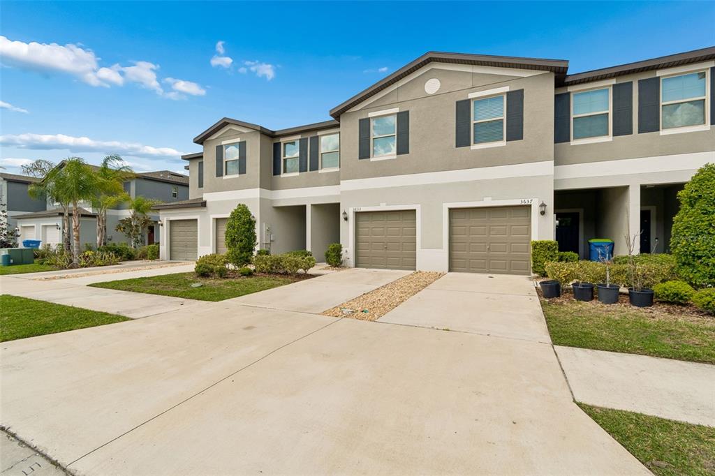 A multi-unit townhouse exterior features beige stucco walls, brown garage doors, and concrete driveways — 3633 BELLMEADE COURT, WESLEY CHAPEL, FL