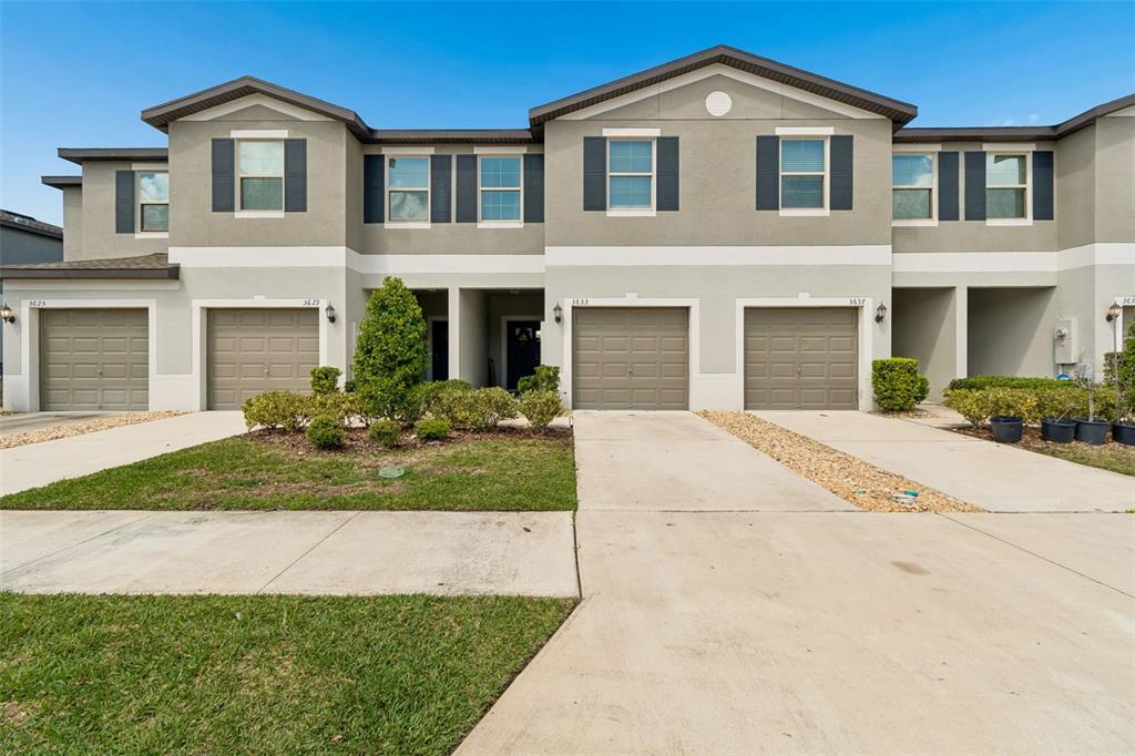 A row of two-story townhomes features beige stucco exteriors, brown garage doors, and concrete driveways — 3633 BELLMEADE COURT, WESLEY CHAPEL, FL