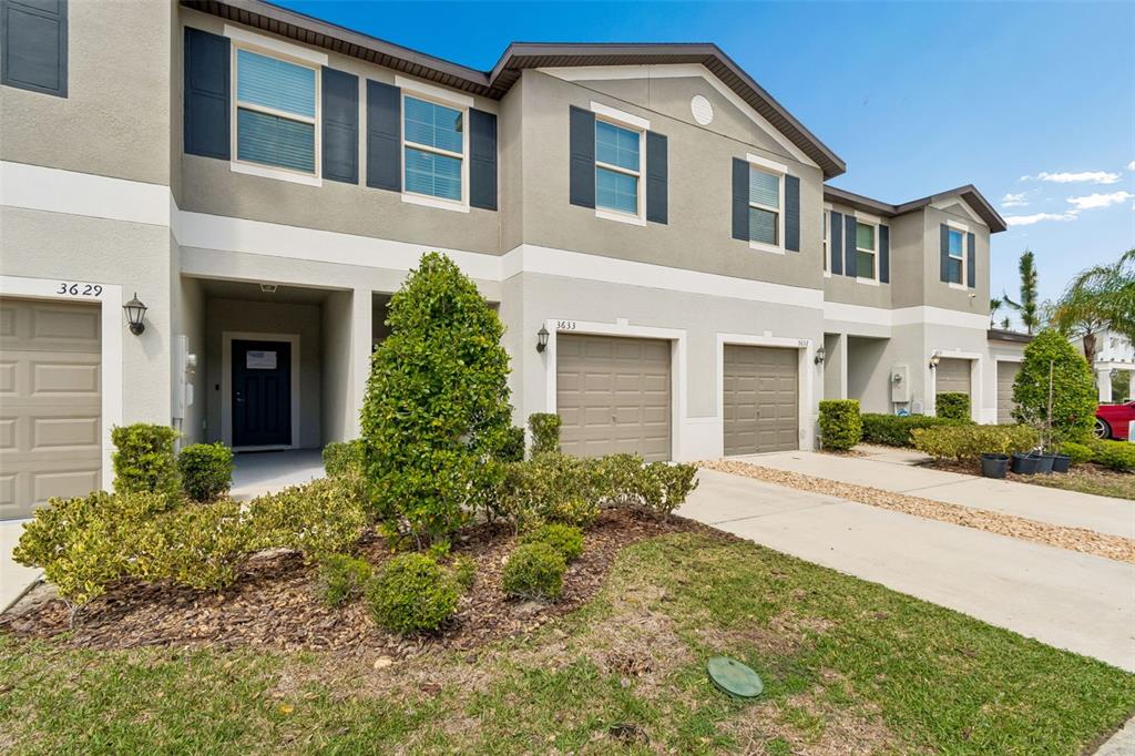 A row of two-story townhomes with beige stucco siding, brown garage doors, and landscaped yards — 3633 BELLMEADE COURT, WESLEY CHAPEL, FL