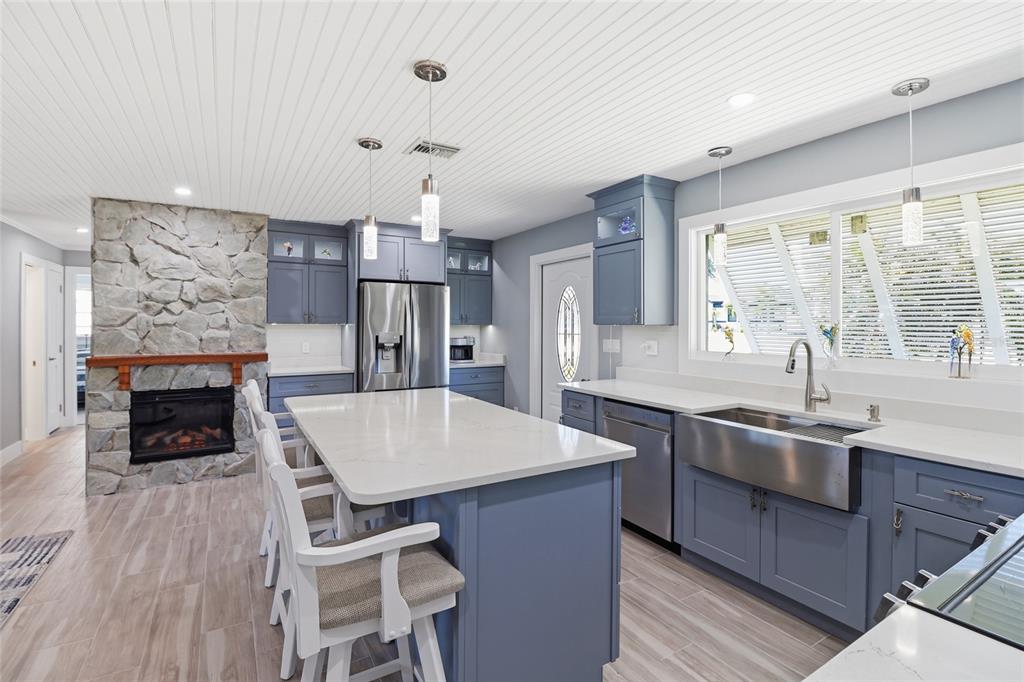 A kitchen features blue cabinets, a stone fireplace, a central island, and stainless steel appliances — 2740 SANIBEL BOULEVARD, ST JAMES CITY, FL