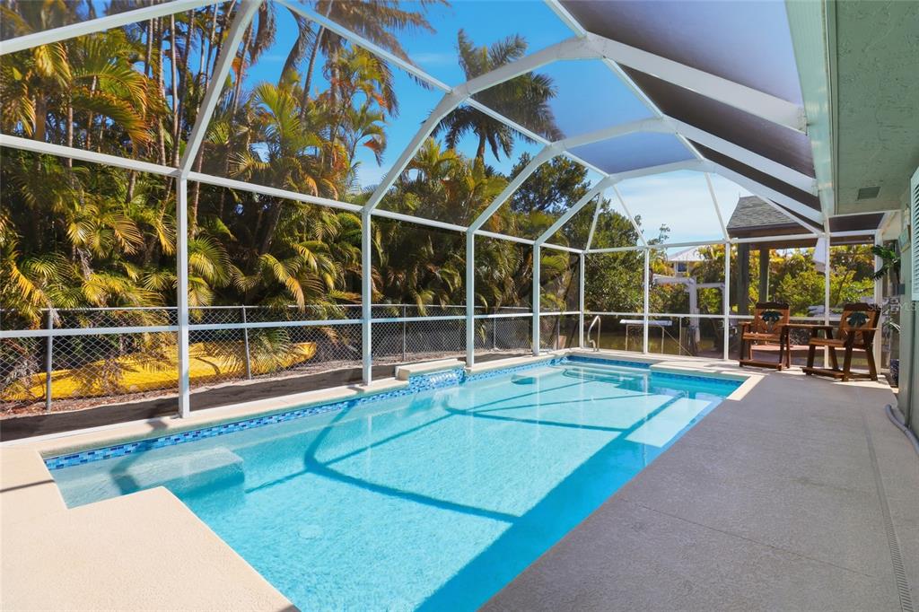 A rectangular swimming pool is enclosed by a white screen cage in a tropical backyard — 2740 SANIBEL BOULEVARD, ST JAMES CITY, FL
