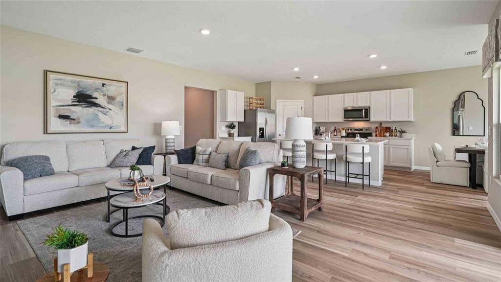 An open-concept living room and kitchen feature light wood flooring and neutral-toned furniture — 17066 NW 179TH WAY, ALACHUA, FL