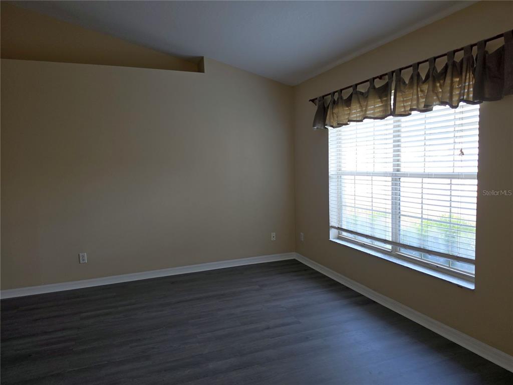 An empty room features beige walls, dark wood-look flooring, and a window with blinds — 1750 NE 40TH STREET, OCALA, FL