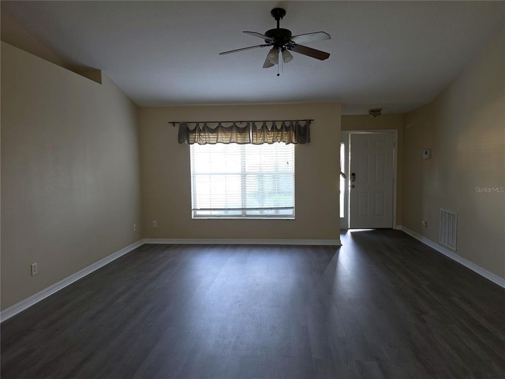 An empty living room features light-colored walls, dark wood-look flooring, and a ceiling fan — 1750 NE 40TH STREET, OCALA, FL