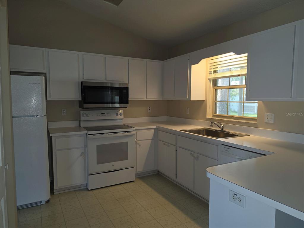 A kitchen with white cabinets, white appliances, laminate countertops, and a window above the sink — 1750 NE 40TH STREET, OCALA, FL