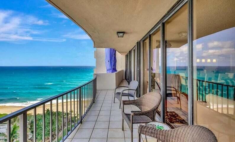 A balcony with wicker chairs overlooks a sandy beach and the blue ocean — 4200 N Ocean Drive # 905, Riviera Beach FL 33404, RIVIERA BEACH, FL