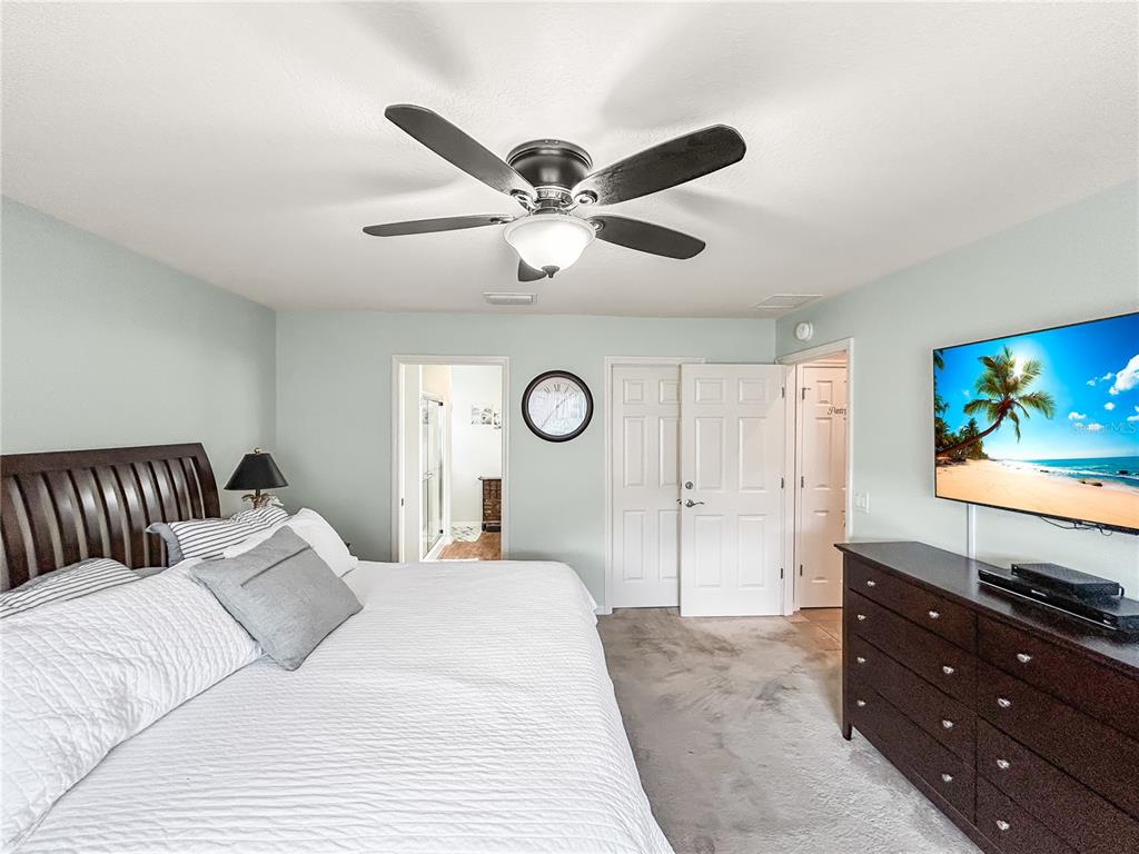 A bedroom features a bed, a ceiling fan, a dresser with a television, and doors — 3737 COSMOS WAY, THE VILLAGES, FL