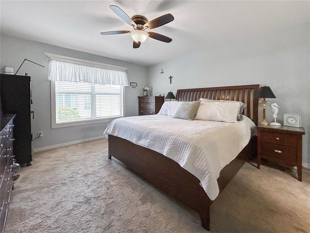 A bedroom features a wooden bed frame, carpeted flooring, a ceiling fan, and a window — 3737 COSMOS WAY, THE VILLAGES, FL