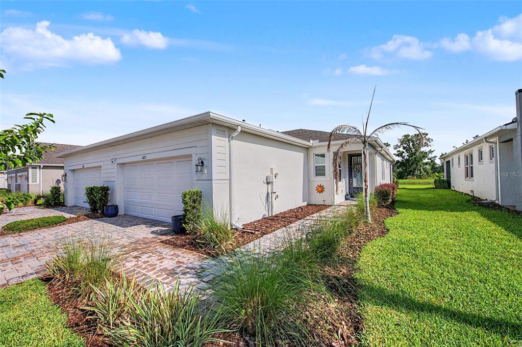 A side view of a single-story house with a white exterior, garage, and paved walkway — 6025 TIMBERDALE AVENUE, WESLEY CHAPEL, FL