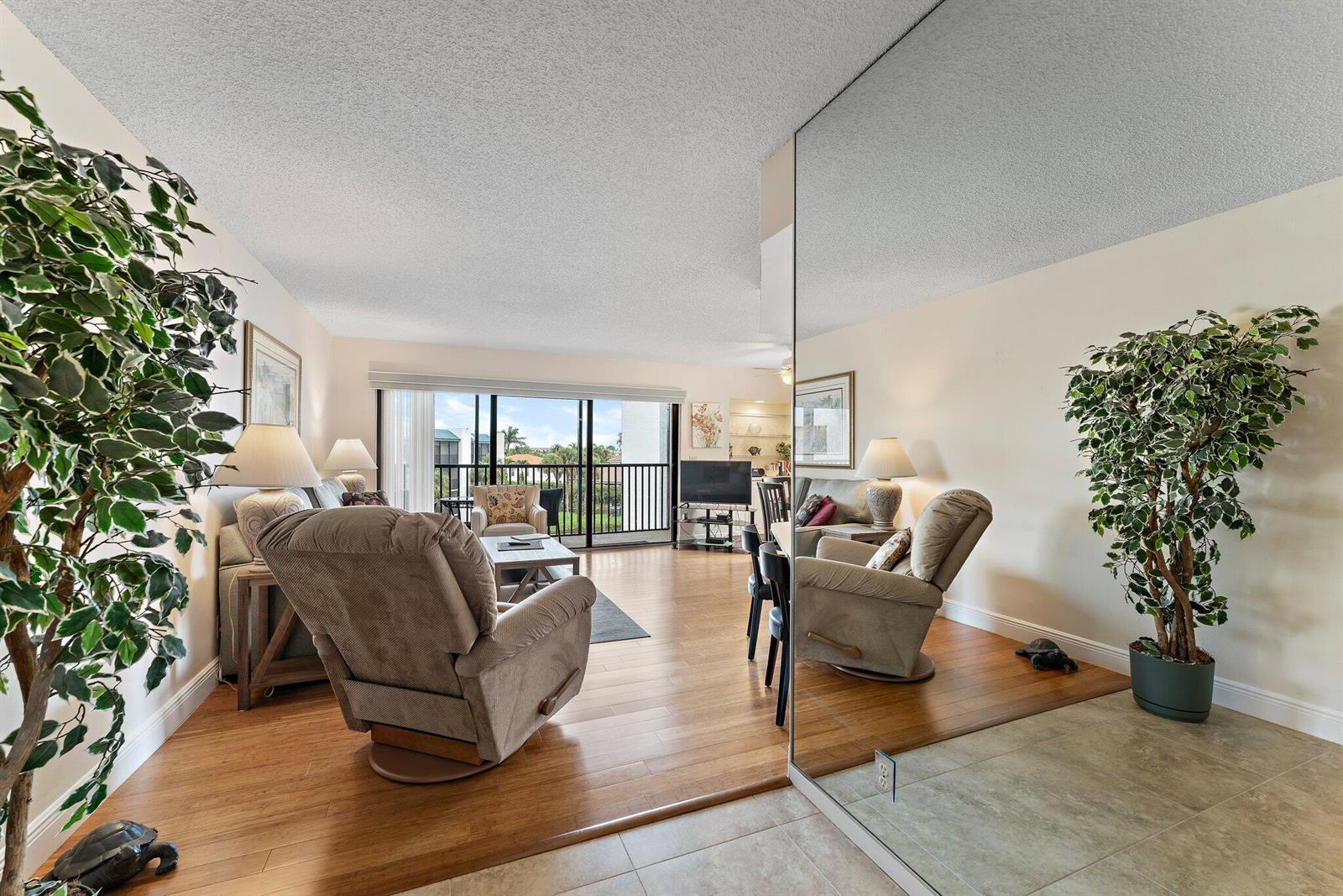 A living room with wood flooring, a large mirror, a recliner, and a balcony view — 1605 S Us Highway 1 # B406, Jupiter FL 33477, JUPITER, FL