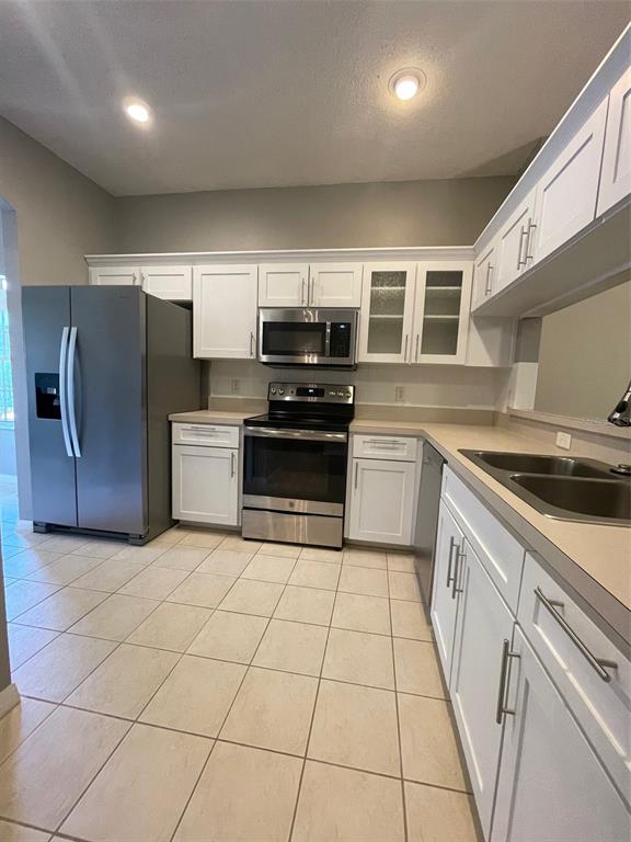 A kitchen features white cabinets, stainless steel appliances, beige countertops, and light-colored tile flooring — 12509 CAVALIER COURT, HUDSON, FL
