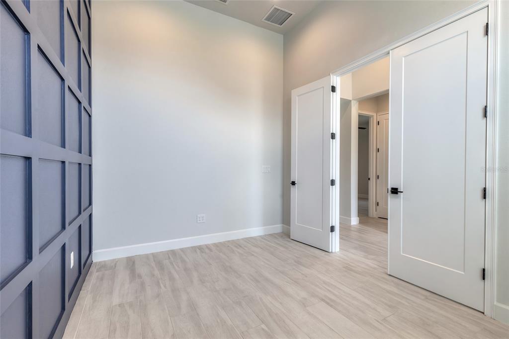 A room with light wood-look flooring, a blue paneled accent wall, and white double doors — 321 AQUAMARINE WAY, DAYTONA BEACH, FL