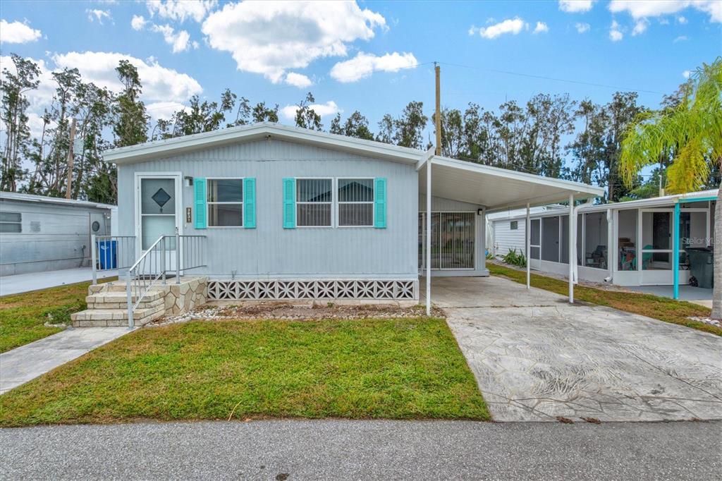 A light blue mobile home features turquoise shutters, a front porch, and a concrete carport — 3831 115TH STREET COURT W, BRADENTON, FL