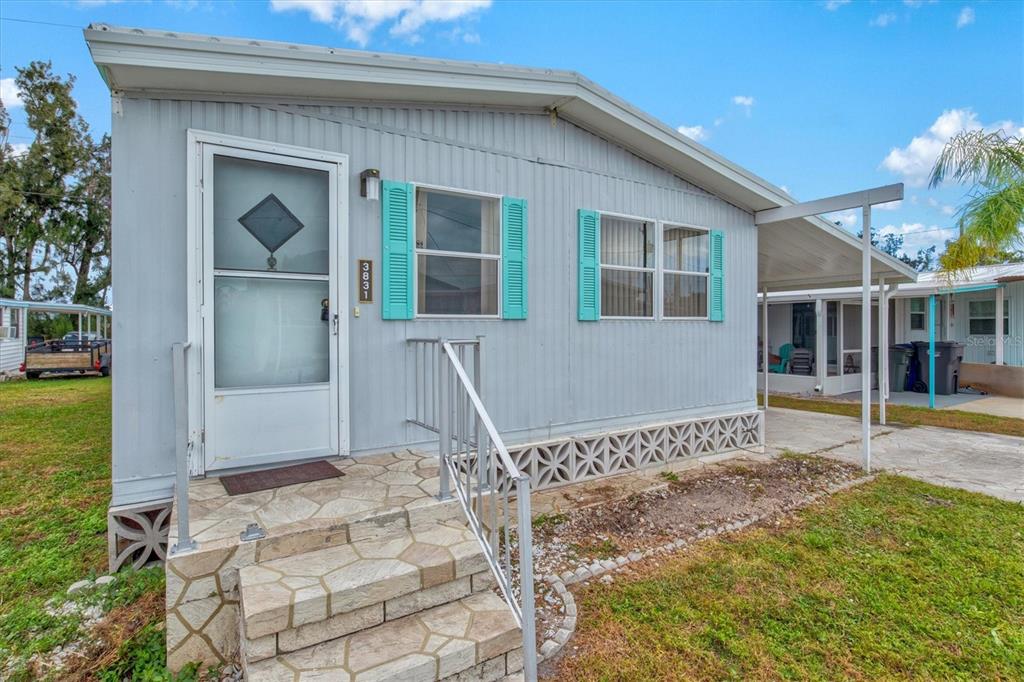 A light blue mobile home features teal shutters, a front porch, and stone-patterned steps — 3831 115TH STREET COURT W, BRADENTON, FL