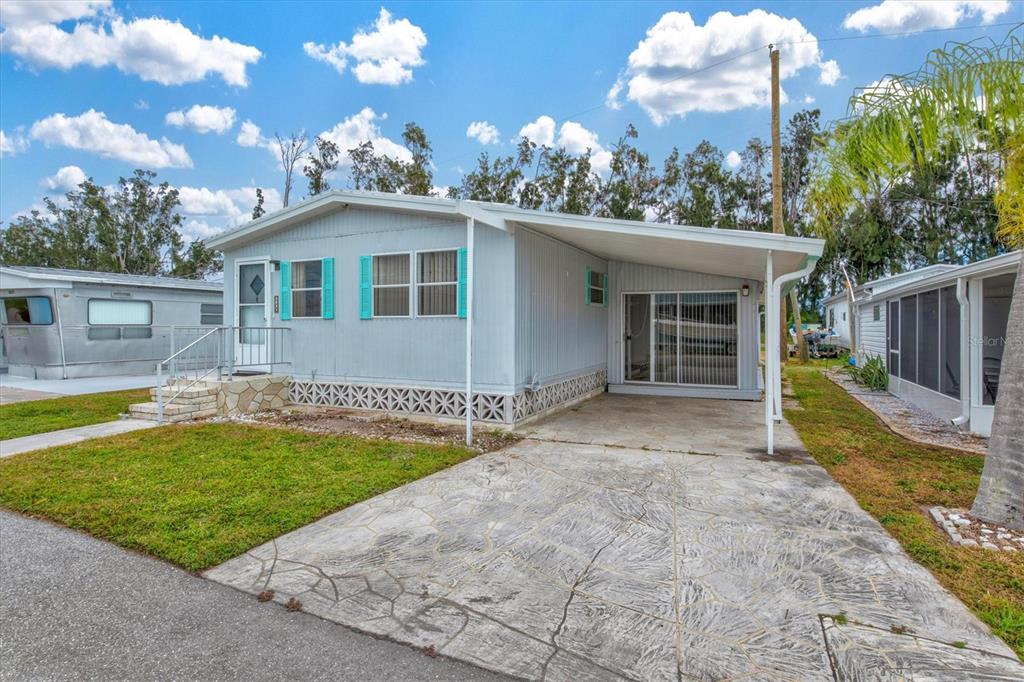 A light blue mobile home with a carport, concrete driveway, and turquoise window shutters — 3831 115TH STREET COURT W, BRADENTON, FL