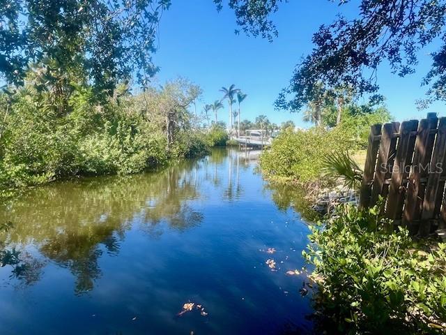 A narrow canal flows through a lush, tree-lined landscape under a clear blue sky — 321 RAVENNA STREET N, NOKOMIS, FL