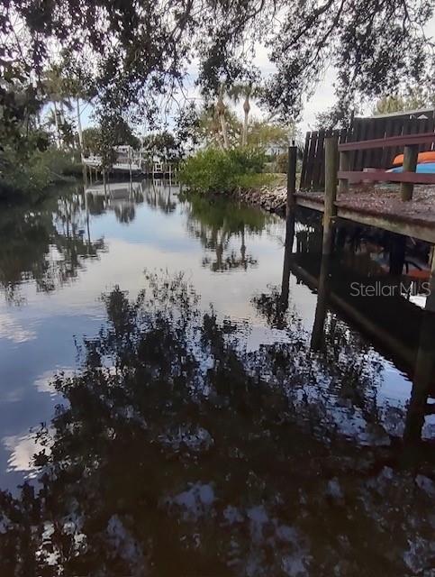 A wooden dock extends over a calm canal surrounded by trees and lush vegetation — 321 RAVENNA STREET N, NOKOMIS, FL