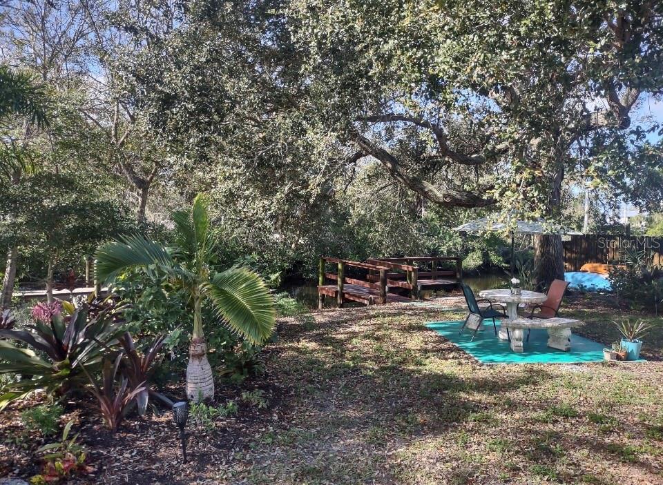 A backyard features a small wooden bridge over a canal, a patio set, and trees — 321 RAVENNA STREET N, NOKOMIS, FL