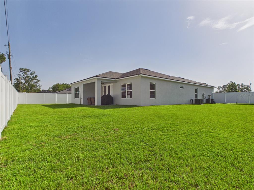 The backyard features a large green lawn, a covered patio, and a white vinyl fence — 15110 SW 43RD AVENUE ROAD, OCALA, FL