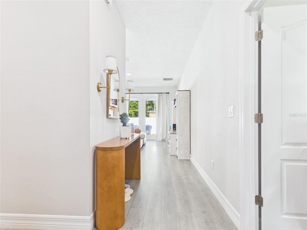 A hallway with light wood-look flooring leads to a living area with glass patio doors — 15110 SW 43RD AVENUE ROAD, OCALA, FL