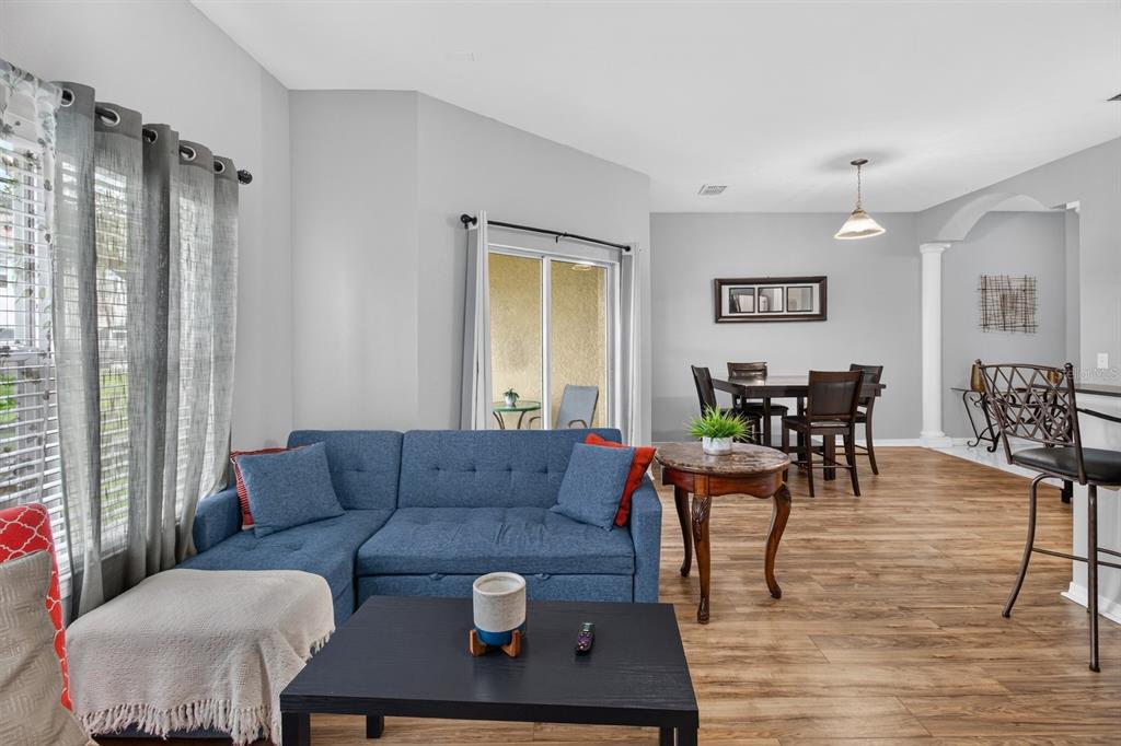 A living room with a blue sectional sofa, wood-look flooring, and an adjacent dining area — 10844 DRAGONWOOD DRIVE, TAMPA, FL