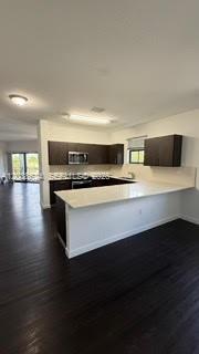 A kitchen with dark cabinets, white countertops, and a breakfast bar overlooks a living area — 15500 SW 136th St. # 211, Miami FL 33196, MIAMI, FL