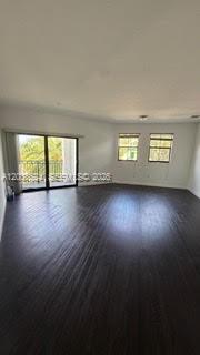 An empty room with dark wood flooring, white walls, and a sliding glass balcony door — 15500 SW 136th St. # 211, Miami FL 33196, MIAMI, FL