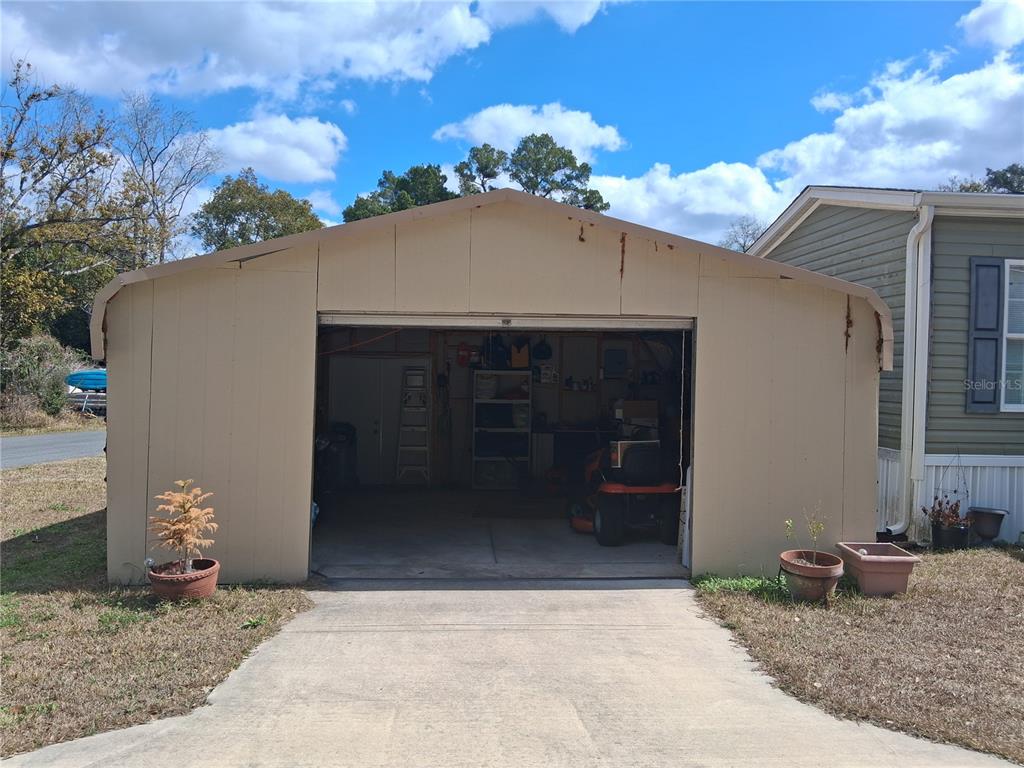 A detached metal garage with a concrete driveway sits next to a light green home — 9170 DAN LYNN STREET, BROOKSVILLE, FL