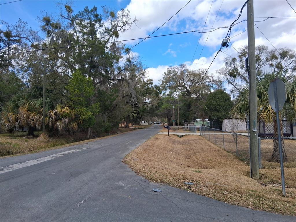 A paved road runs through a residential area with mature trees and a chain-link fence — 9170 DAN LYNN STREET, BROOKSVILLE, FL