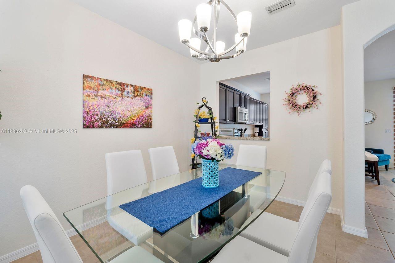 A dining room features a glass table, white chairs, a chandelier, and a kitchen pass-through — 2851 W Prospect Rd # 1306, Tamarac FL 33309, TAMARAC, FL