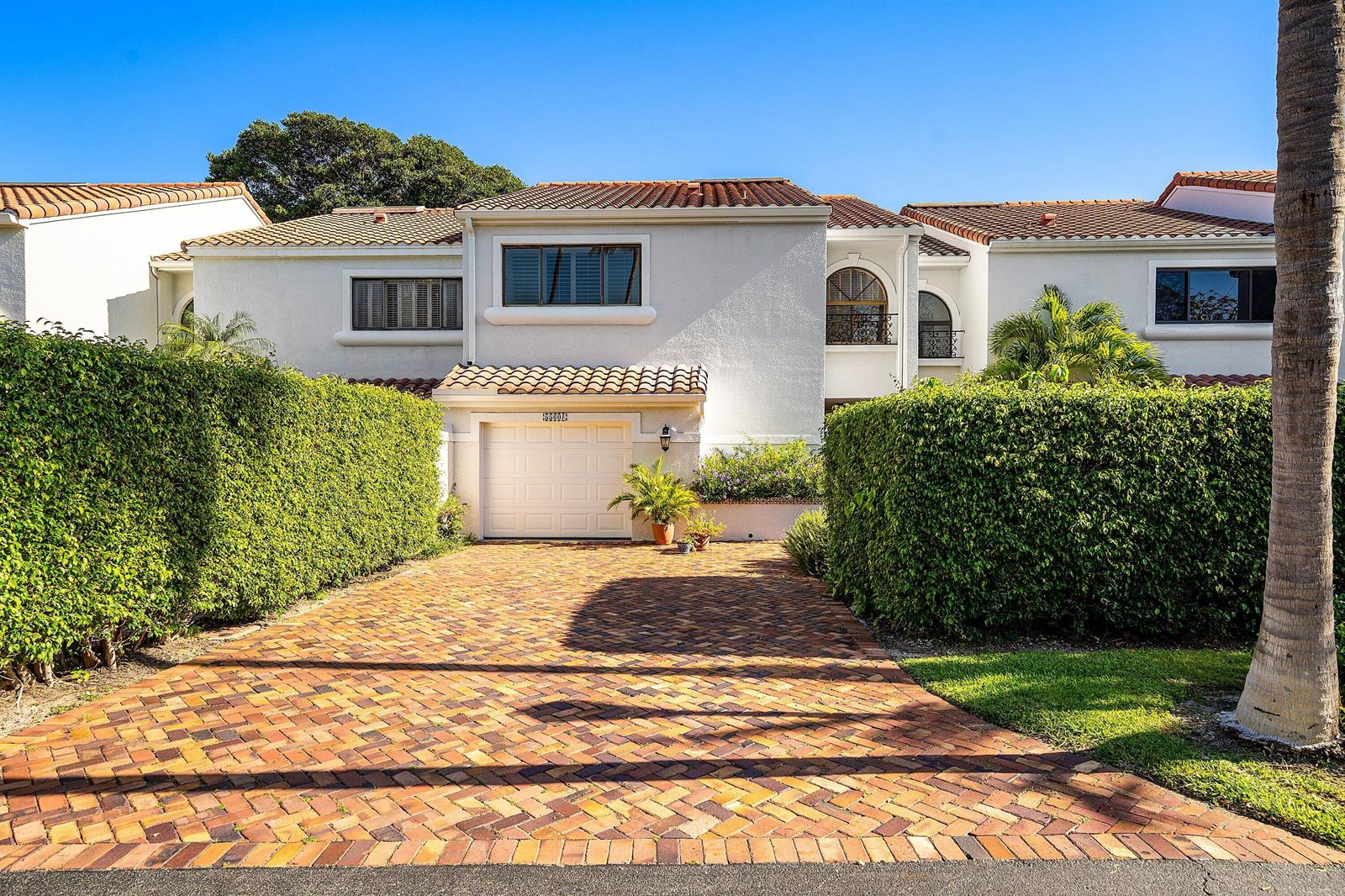 A two-story white stucco townhouse features a brick driveway, a garage, and tall privacy hedges — 5560 N Ocean Boulevard # A, Ocean Ridge FL 33435, OCEAN RIDGE, FL