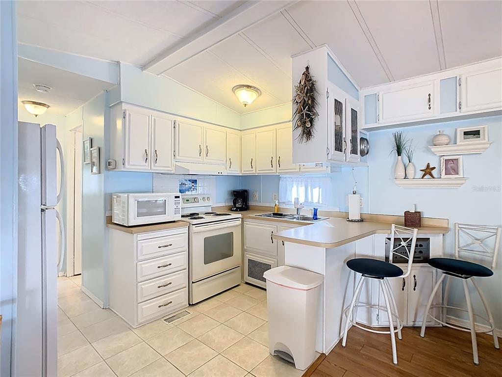 A kitchen features white cabinets, light countertops, a white stove, and a breakfast bar — 9000 US HWY 192 UNIT 293, CLERMONT, FL