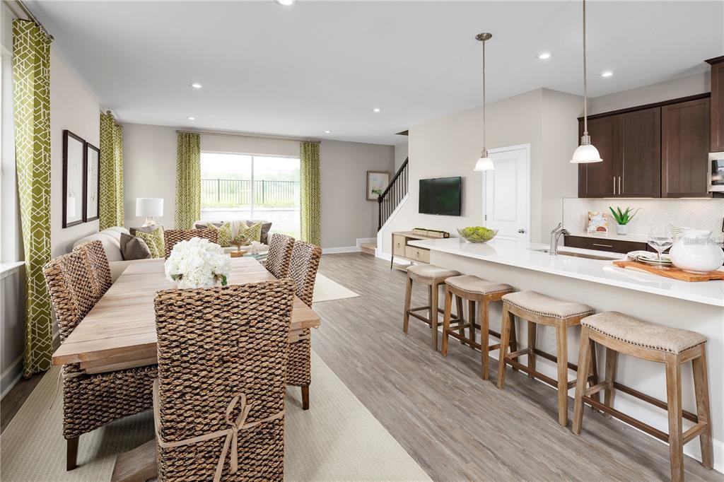 An open-concept dining area and kitchen feature woven chairs, a breakfast bar, and wood flooring — 6712 CEDAR LANDING CIRCLE, LEESBURG, FL