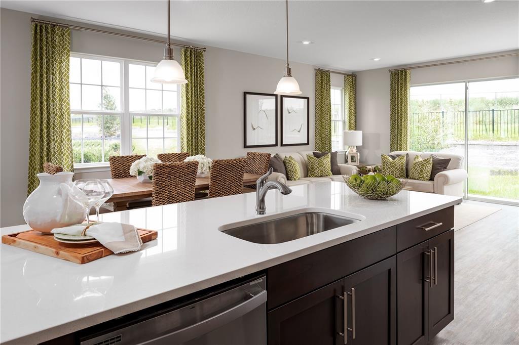 A kitchen island with a stainless steel sink overlooks an open-concept dining and living area — 6712 CEDAR LANDING CIRCLE, LEESBURG, FL