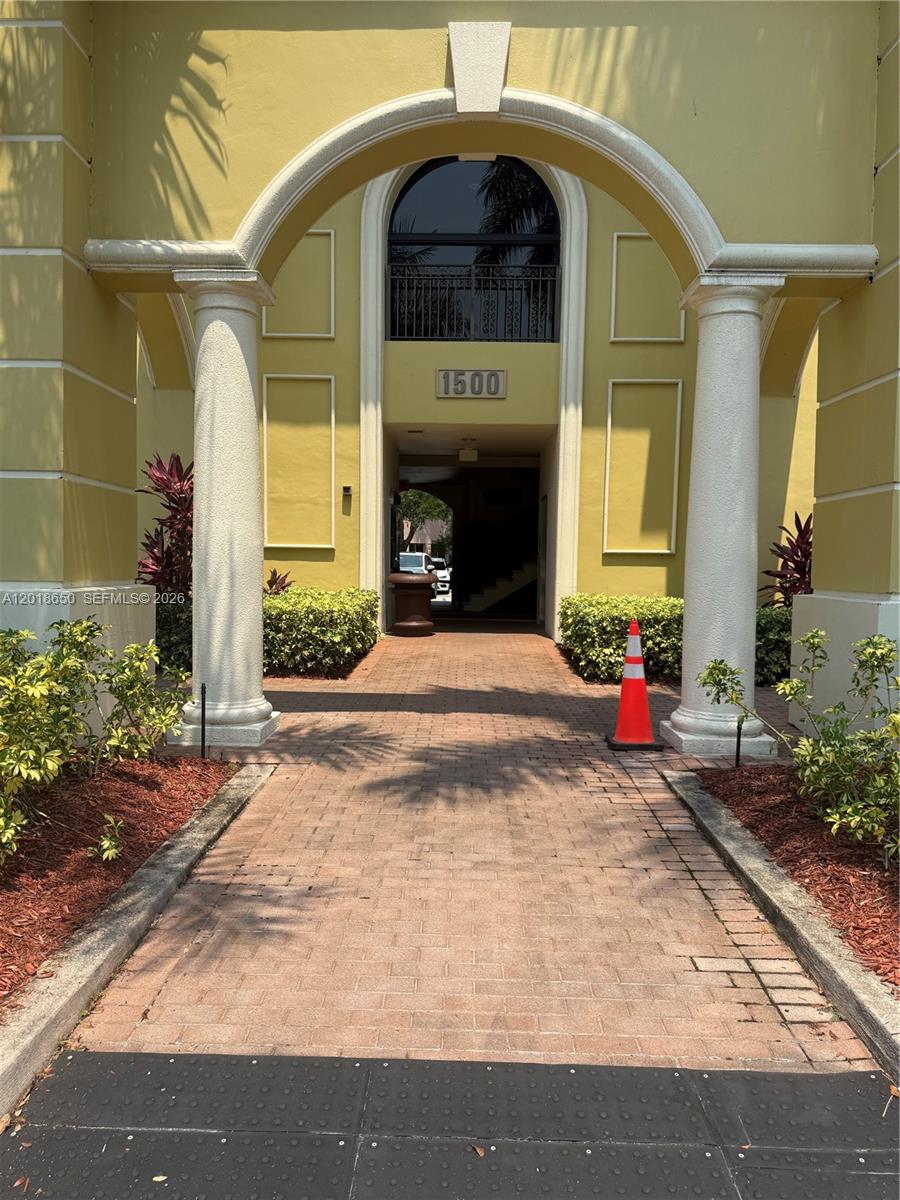 A brick walkway leads through a large arched entryway toward the entrance of building 1500 — 1528 Weston Rd, Weston FL 33326, WESTON, FL