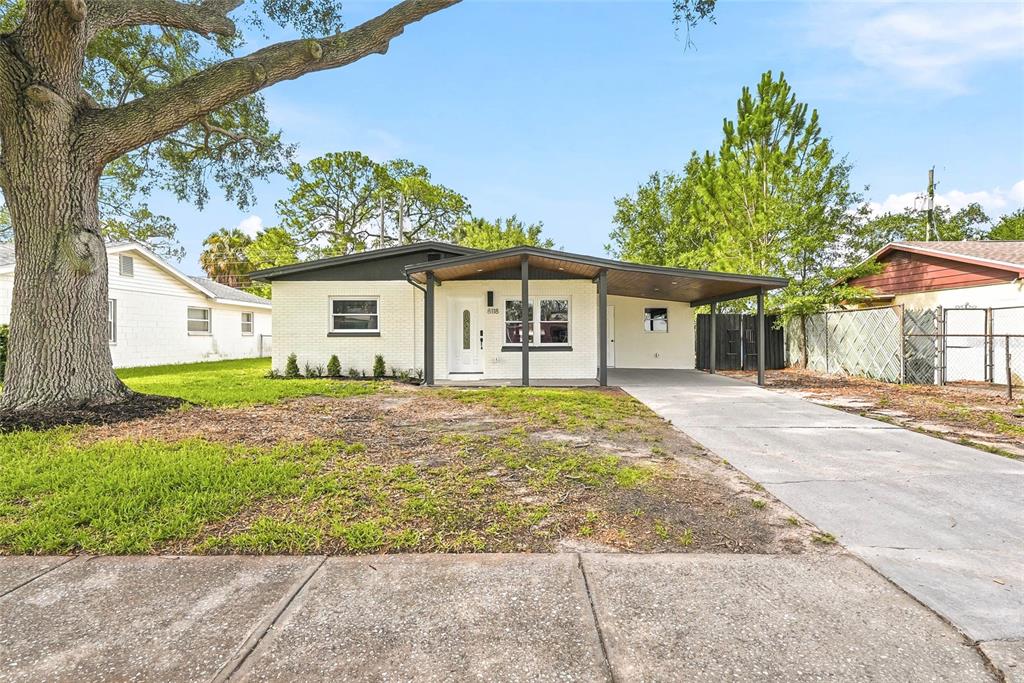 A single-story white brick house features a dark roof, a carport, and a large tree — 8118 TANGLEWOOD LANE, TAMPA, FL