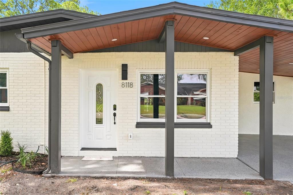 A white brick house exterior features a covered porch, a white front door, and windows — 8118 TANGLEWOOD LANE, TAMPA, FL