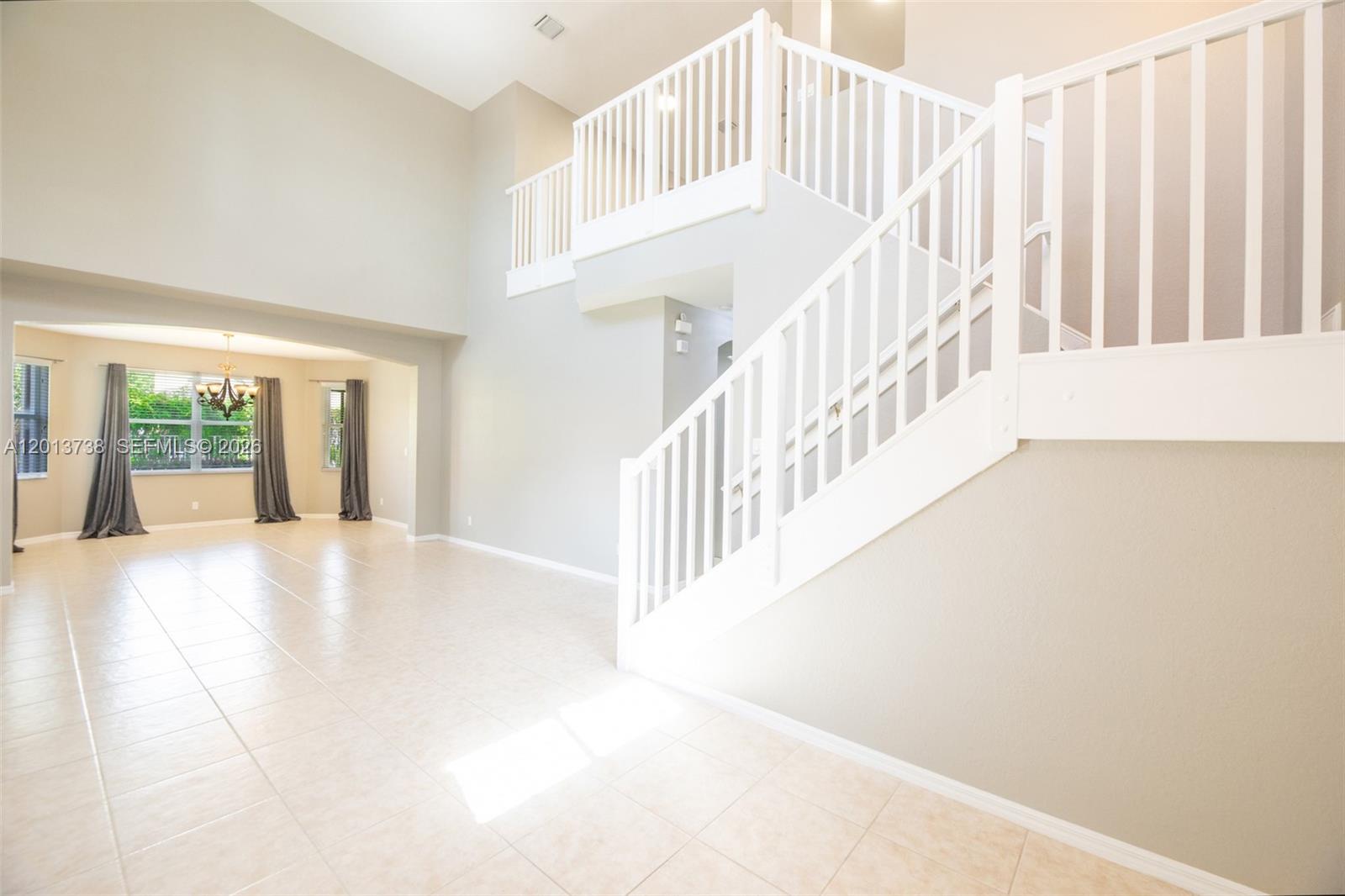 A bright, open-concept foyer features a white staircase, a balcony landing, and tile flooring — 4207 W Whitewater Ave, Weston FL 33332, WESTON, FL