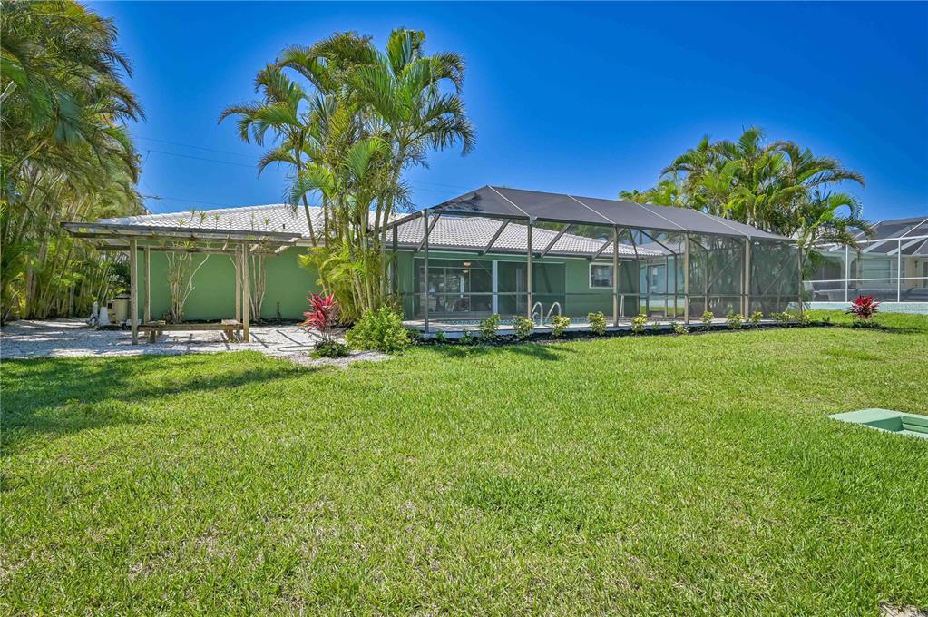 A backyard view of a green house with a screened-in pool enclosure and pergola — 4815 SORRENTO COURT, CAPE CORAL, FL