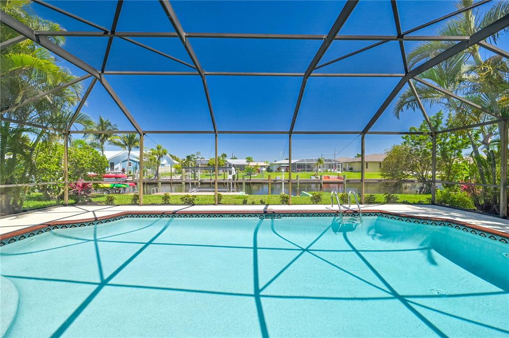 A swimming pool enclosed by a screen cage overlooks a canal with a boat dock — 4815 SORRENTO COURT, CAPE CORAL, FL