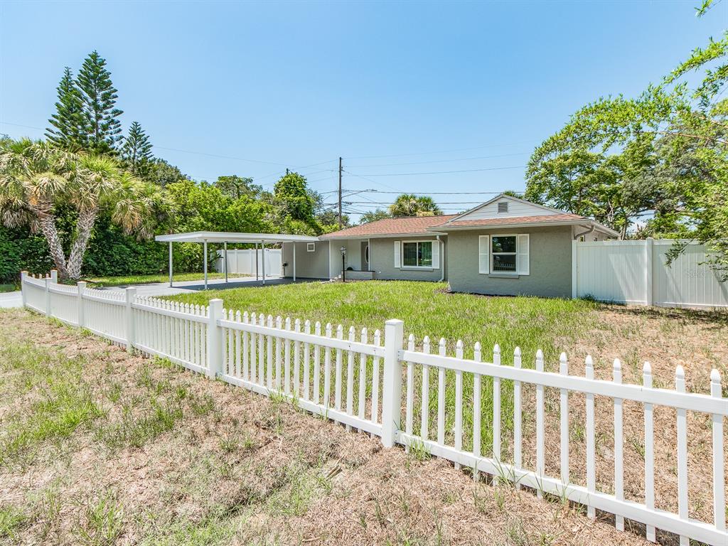 A single-story house with a carport sits behind a white picket fence — 502 LEXINGTON STREET, DUNEDIN, FL