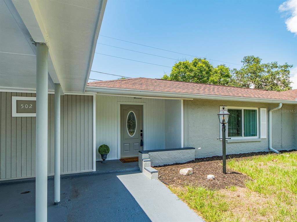 A gray front door with a decorative window sits under a covered entryway at 502 — 502 LEXINGTON STREET, DUNEDIN, FL