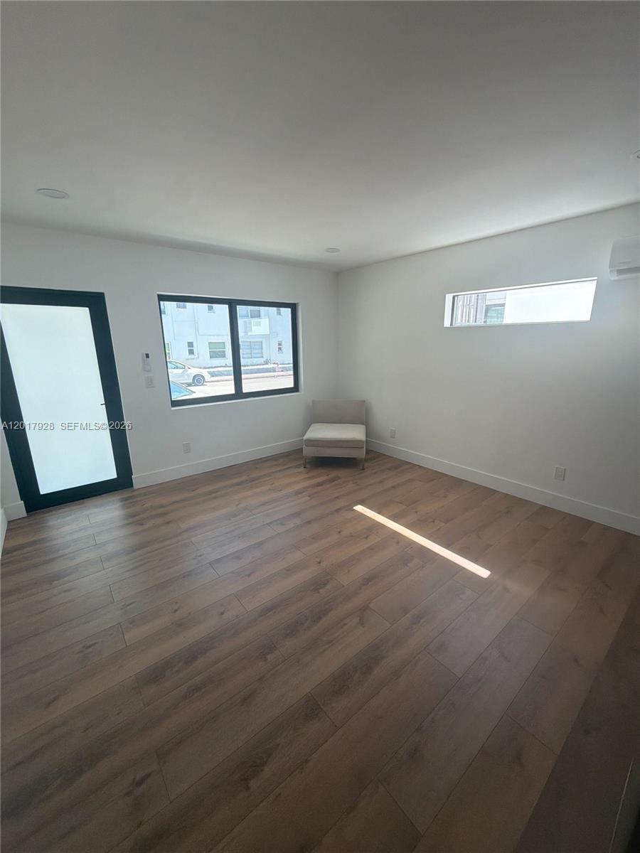 A minimalist room features wood-look flooring, white walls, a glass door, and two windows — 7801 Byron Ave # 1, Miami Beach FL 33141, MIAMI BEACH, FL