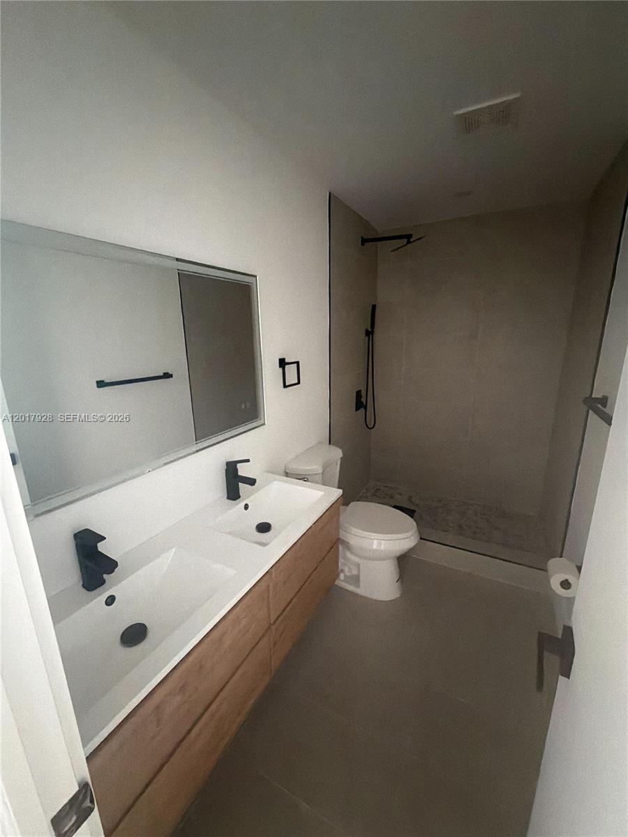 A modern bathroom features a double vanity with wood cabinets, black fixtures, and a shower — 7801 Byron Ave # 1, Miami Beach FL 33141, MIAMI BEACH, FL